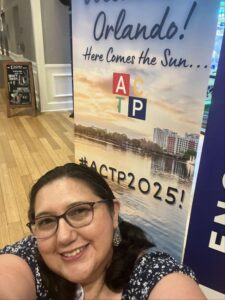 A woman sitting in front of a sign that says " # actp 2 0 2 5 ".