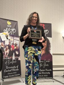 A woman holding an award standing in front of two posters.