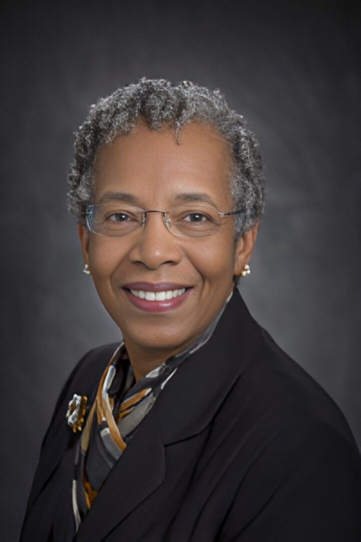 Smiling person with glasses and gray hair.